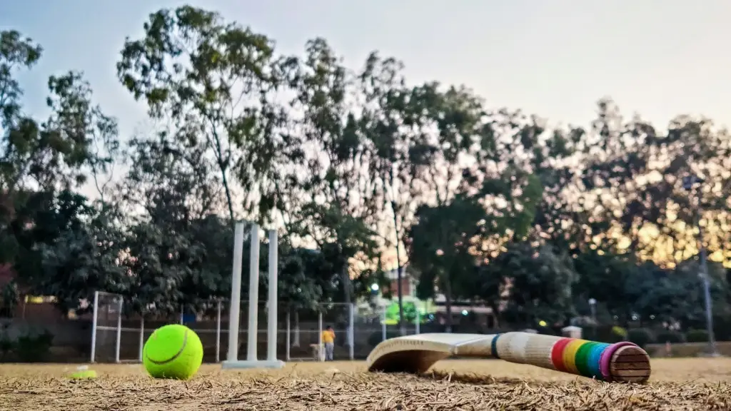 Cricket bat and ball on a pitch with stumps in the background